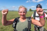 Female tandem student in a green shirt raises her fists in excitement after landing from her skydive.