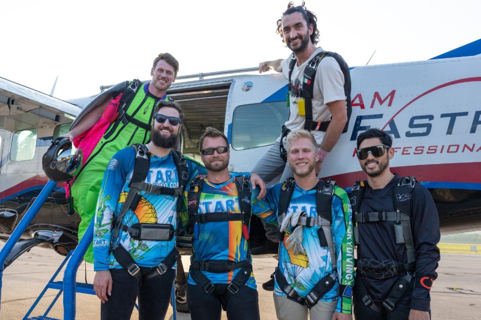 Group of male skydivers pose before boarding the plane for a jump.