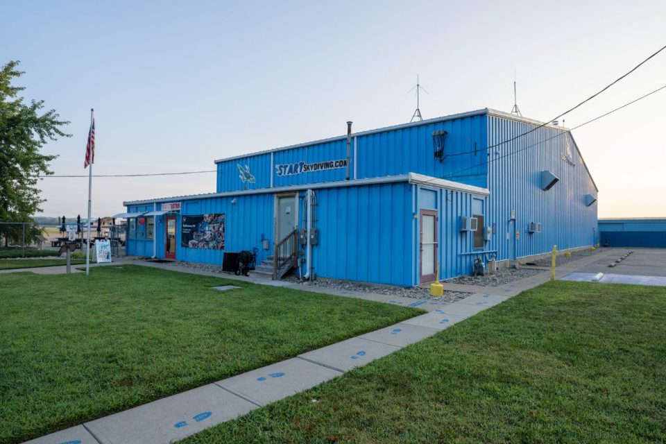 Outside few of Start Skydiving metal office building and blue aircraft hangar