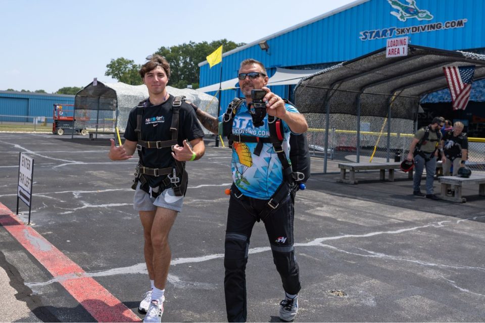 Tandem skydiver and his instructor smile and walk toward the airplane.