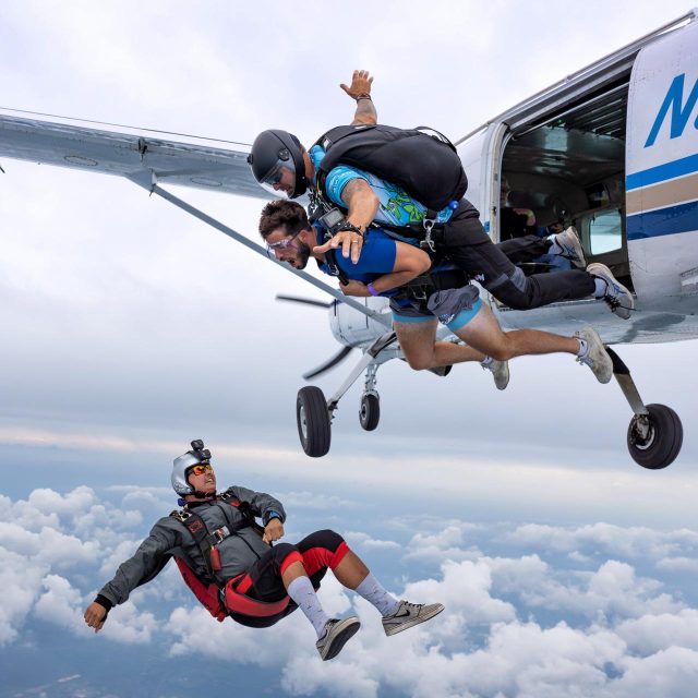 Airplane exit shot of a tandem pair and their videographer below.