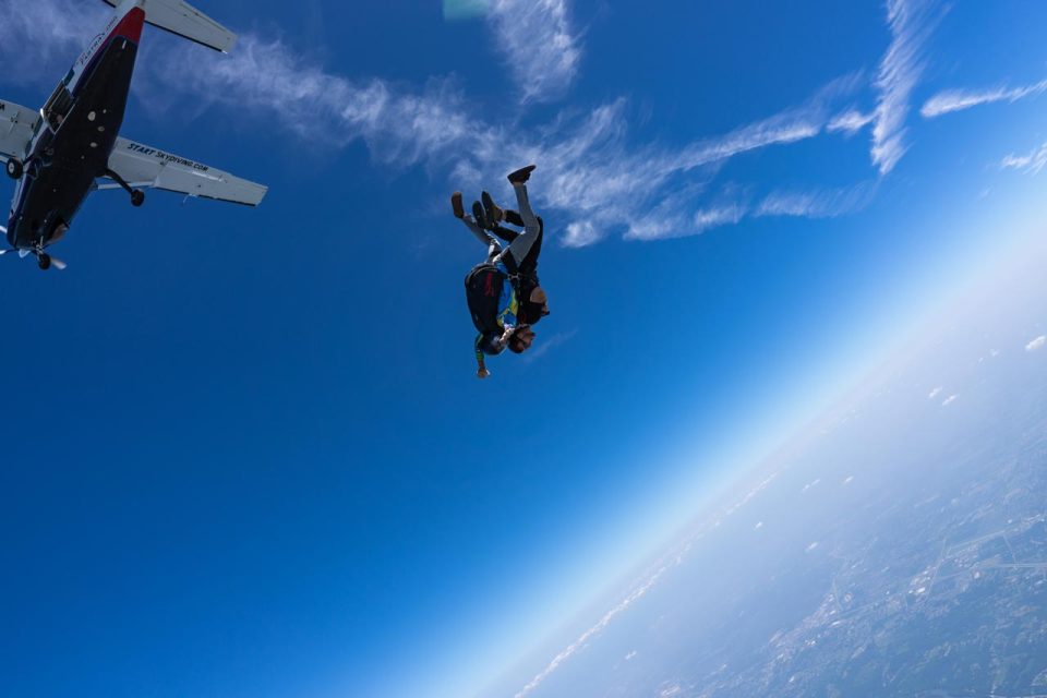 Tandem skydivers shortly after exiting the aircraft. Blue skies and skydiving airplane in the background.
